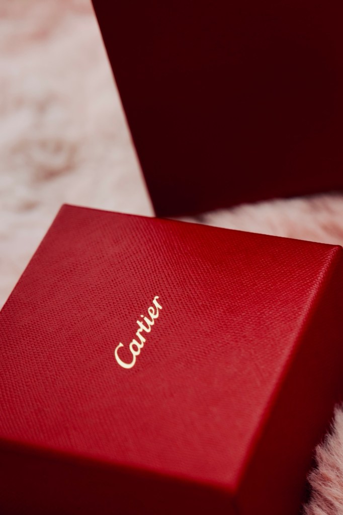 Red Cartier jewelry box with gold script logo on a soft pink background