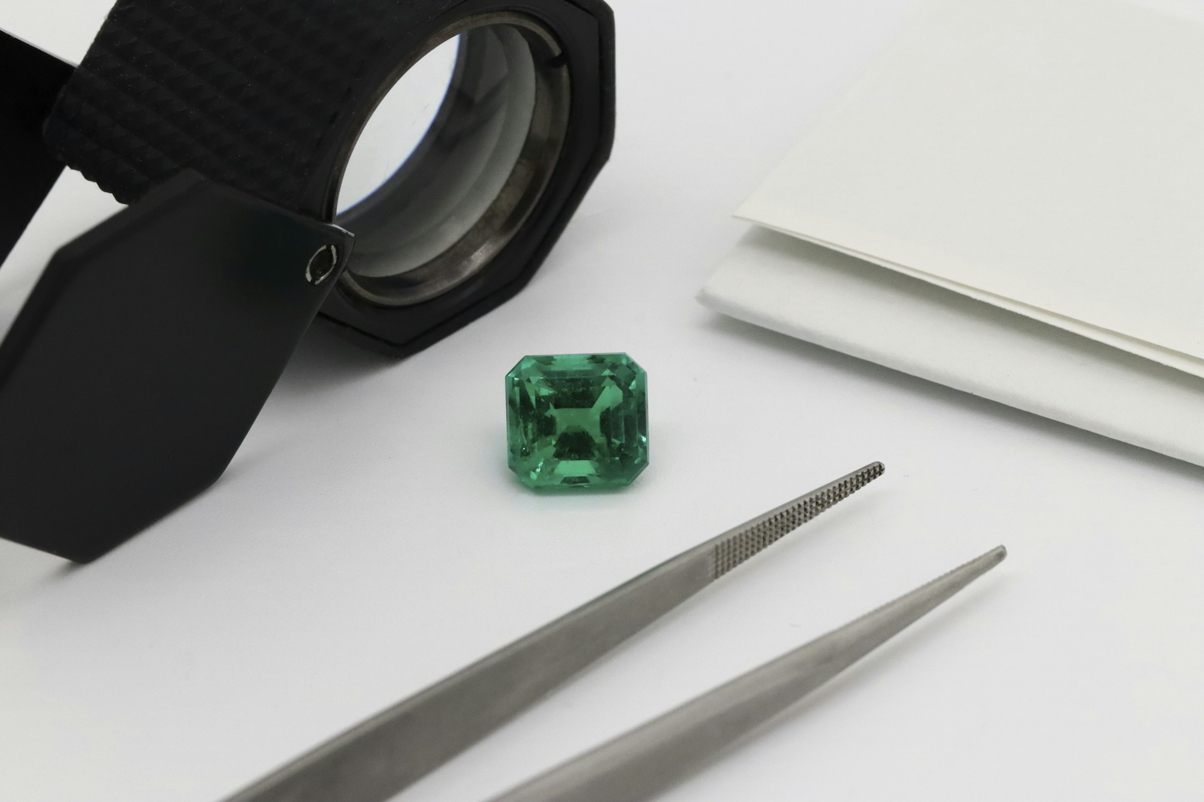 Faceted green gemstone with a jeweler's loupe and tweezers (stock photo)