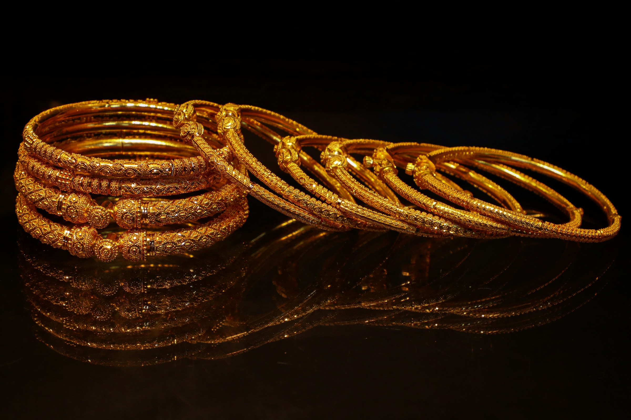 Stack of ornate gold bangles on a dark reflective surface